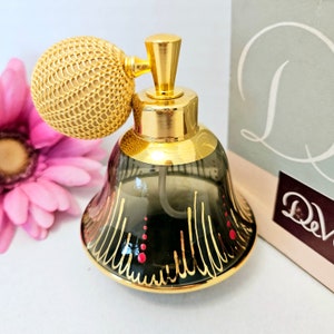 May include: A gold and black perfume bottle with a decorative design. The bottle has a gold atomizer and a gold cap with a woven design.