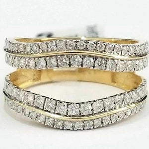 Puede incluir: Juego de dos anillos dorados con diseño de onda. Cada anillo presenta una fila de pequeñas piedras preciosas transparentes. Los anillos están sobre un fondo blanco, resaltando el brillo de las piedras.