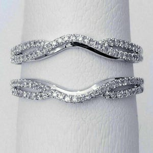 May include: Two curved, silver rings set with small, clear gemstones. The rings have a wave-like design, with the gemstones set along the curves. These rings are likely wedding bands or engagement ring enhancers.
