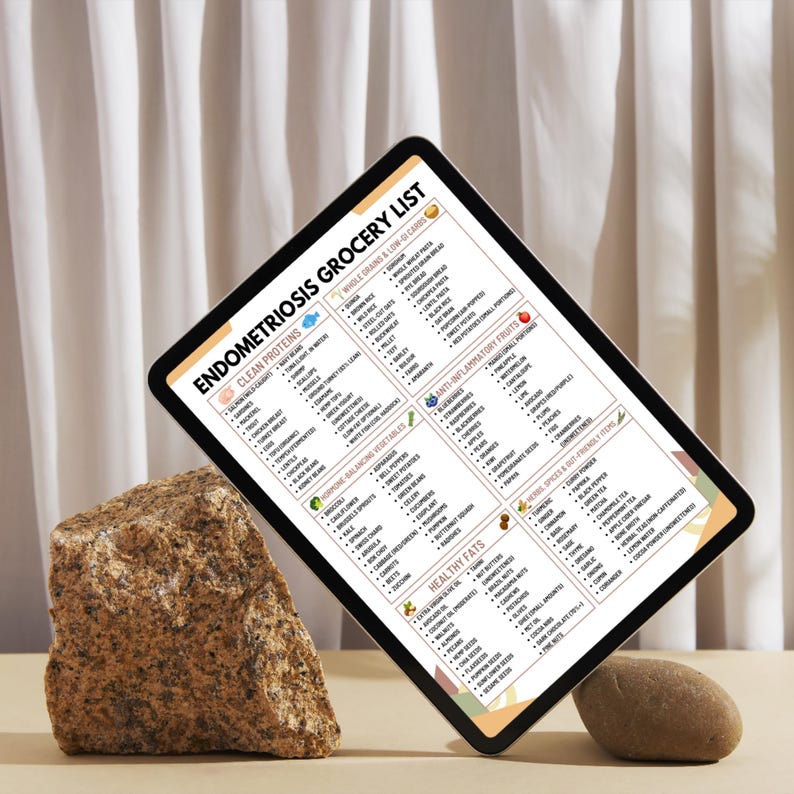 May include: A digital tablet displaying an "Endometriosis Grocery List" with categories like Clean Proteins, Anti-Inflammatory Fruits, and Healthy Fats. The tablet is angled, with a neutral background and two stones.