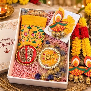 May include: A white gift box labeled Happy Diwali containing a yellow fabric pouch with lotus prints, a red circular ornament with beaded footprints, a yellow circular ornament with the Hindi text Labh, and decorative paper diya hangings.
