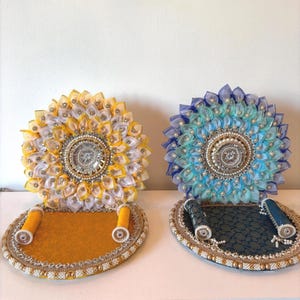 Puede incluir: Dos soportes decorativos circulares con arreglos de tela en forma de p&eacute;talos verticales, amarillo y blanco a la izquierda, y azul y turquesa a la derecha. Cada soporte tiene un adorno central con cuentas y dos peque&ntilde;os cilindros.