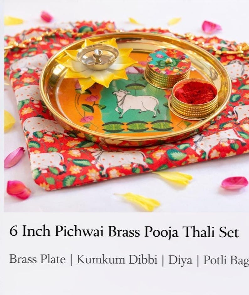 May include: A 6-inch brass pooja thali set featuring a round brass plate with a central cow illustration, a yellow lotus-shaped diya, and a small lidded container filled with red kumkum powder, all resting on a red fabric potli bag with cow motifs.