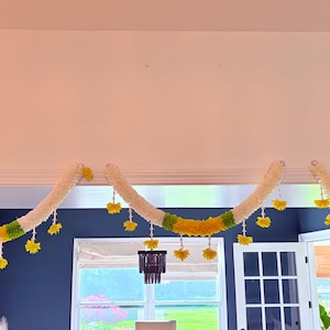 May include: A decorative garland with a white, yellow, and green color scheme. The garland is suspended from the ceiling and features a repeating pattern of white sections, yellow flowers, and green accents. The garland is a festive decoration.