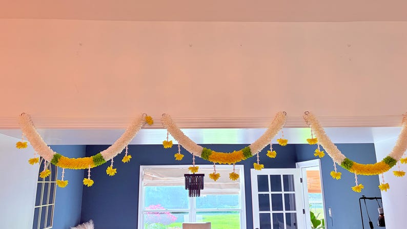 May include: A decorative garland with a white, yellow, and green color scheme. The garland is suspended from the ceiling and features a repeating pattern of white sections, yellow flowers, and green accents. The garland is a festive decoration.