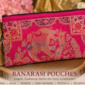 May include: A rectangular fuchsia pink pouch featuring a woven gold and purple elephant motif and floral patterns. The pouch has a black zipper closure with a gold tassel attached to the side. The text BANARASI POUCHES is printed below.