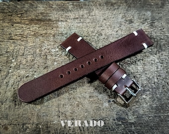 May include: A pair of brown leather watch straps with white stitching. The straps have a silver buckle and are displayed on a weathered wooden surface. The word "VERADO" is visible at the bottom.