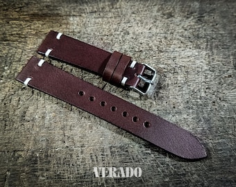 May include: A pair of dark burgundy leather watch straps with white stitching. The straps have a silver buckle and are displayed on a wooden surface. The word "VERADO" is printed at the bottom.