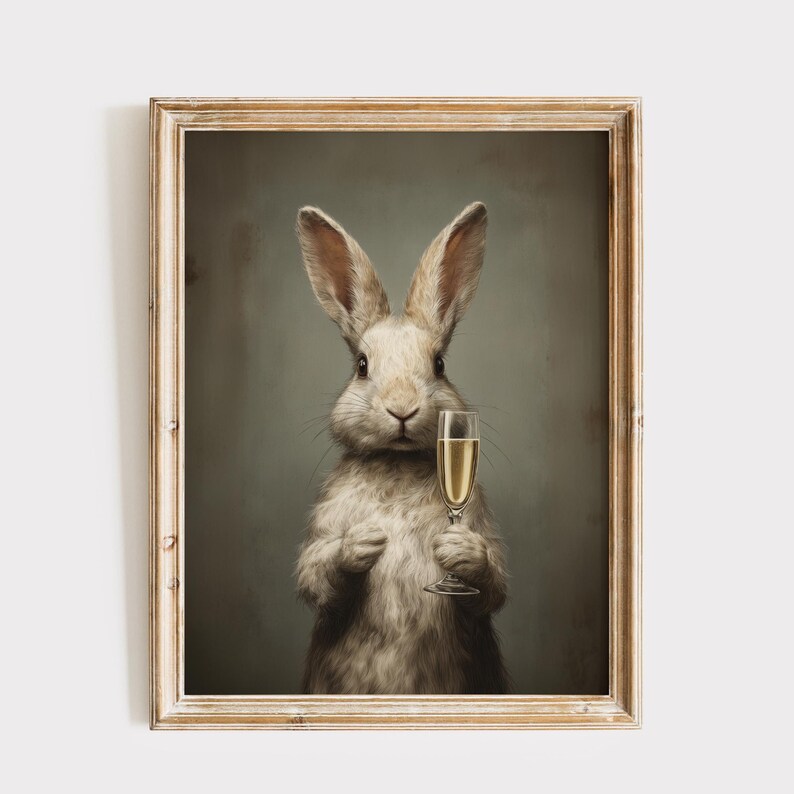 May include: A framed print featuring a rabbit holding a champagne flute. The rabbit has light gray fur and is set against a muted green background. The champagne in the glass is a golden color, and the frame is a light wood tone.