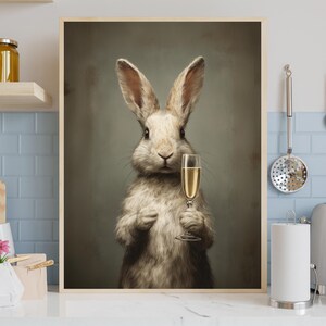 May include: A framed print featuring a rabbit holding a champagne flute. The rabbit has light brown fur and long ears. The champagne glass is filled with a golden liquid. The background is a muted green.