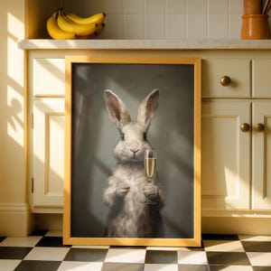 May include: A framed print featuring a rabbit holding a champagne flute. The rabbit has light gray fur and long ears. The frame is a light wood color. The background is a muted gray. The print is displayed in a kitchen setting.