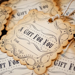 May include: Close-up of several vintage-style gift tags. Each tag is scalloped-edged, with the words "A GIFT FOR YOU" printed in a classic font. The tags have space for "To" and "From" and are tied with twine.