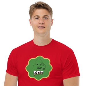 Könnte beinhalten: Ein rotes T-Shirt mit einer grün-gelben Grafik. Die Grafik zeigt eine Pudel-Illustration und den Text "PITT poodle" in Weiß. Das T-Shirt ist aus einem weichen Material gefertigt.