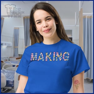 May include: A royal blue t-shirt with the text "MAKING NURSE" in a colorful, multi-font design. The shirt is worn by a person in a hospital setting. The Tee Woo logo is in the upper left corner.