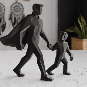May include: A black geometric sculpture of a person holding hands with a child. The adult figure wears a cape. The figures are walking forward. The sculpture is on a white surface with a marble pattern.