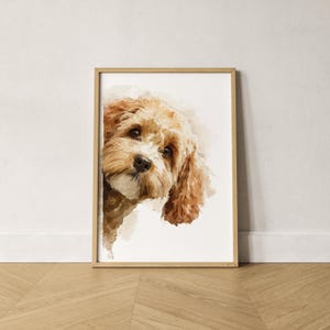 May include: A framed watercolour print of a dog with light brown fur and floppy ears. The dog is peeking out from behind a white surface, with a soft, artistic style. The frame is made of light-coloured wood.