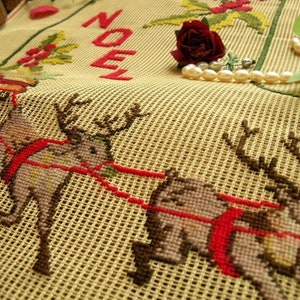 May include: A beige canvas with a red "NOEL" embroidered on it. Two reindeer are embroidered on the canvas, pulling a red sled. The reindeer are brown and gray with red harnesses. A red rose and a pearl necklace are on the canvas.