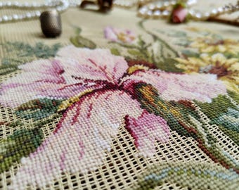 Könnte beinhalten: Nahaufnahme eines floralen Nadelspitzendesigns mit einer großen rosa und lila Blume mit grünen Blättern und gelben Akzenten. Ein Fingerhut und Perlen befinden sich im Hintergrund. Die Nadelspitze befindet sich auf einem beigen Netz.
