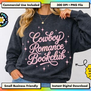 May include: A dark charcoal gray crewneck sweatshirt featuring the light pink text Cowboy Romance Bookclub in a cursive script font, surrounded by small pink four-pointed star icons. The design is centered on the front of the garment.