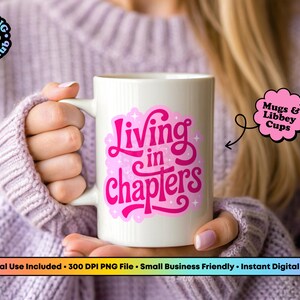 May include: A white ceramic mug featuring a vibrant pink graphic design with the text "Living in chapters" in a stylized script font, accented by small star shapes. The design is centered on the front of the mug, which has a smooth finish.