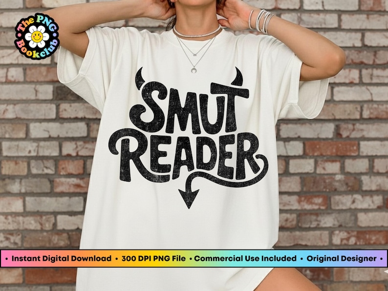 May include: Off-white t-shirt with the text "SMUT READER" in a distressed black font. The design includes devil horns above the word "SMUT" and an arrow pointing down below "READER". The shirt is a casual style.
