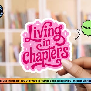 May include: A die-cut sticker featuring the text Living in chapters in a bold, dark pink script font with a light pink outline and small white star accents. The sticker has a wavy, cloud-like border and is presented against a blurred background.