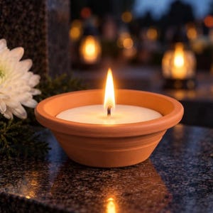 Könnte beinhalten: Eine Terrakottaschale mit einer weißen Wachskerze und brennender Flamme. Die Kerze steht auf einer dunklen, polierten Steinoberfläche neben einer weißen Blume. Die Schale hat einen breiten, flachen Rand und einen sich verjüngenden Boden.