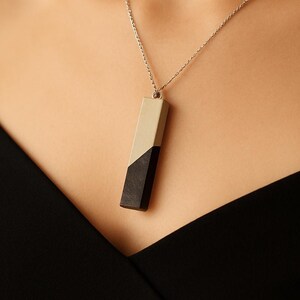May include: A silver chain necklace with a rectangular pendant. The pendant is split diagonally, with a beige top half and a black bottom half. The necklace is worn against a black top.