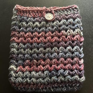 Könnte beinhalten: Handgefertigte Häkeltasche in Lila-, Grau- und Rosatönen. Die Tasche hat ein strukturiertes Stichmuster und einen Knopfverschluss. Der obere Rand ist in einem dunkleren Lilaton gehalten. Geeignet zum Schutz kleiner elektronischer Geräte oder anderer Gegenstände.