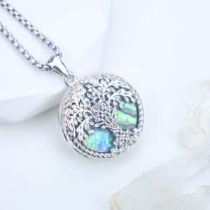 May include: A silver-toned pendant necklace featuring a round pendant with a tree of life design. The pendant has an abalone shell inlay with iridescent blue and green hues. The necklace chain is a matching silver color.