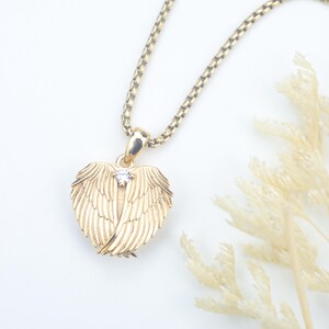 Puede incluir: Un collar con colgante dorado con un dise&ntilde;o en forma de coraz&oacute;n con alas de &aacute;ngel. Una peque&ntilde;a gema transparente est&aacute; engastada en el centro del colgante. La cadena del collar tambi&eacute;n es dorada y tiene un patr&oacute;n texturizado y enlazado.