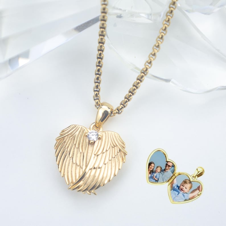 Puede incluir: Collar con colgante en forma de coraz&oacute;n dorado con dise&ntilde;o de alas de &aacute;ngel. El relicario tiene una peque&ntilde;a piedra con forma de diamante en el centro y se abre para revelar una foto. La cadena del collar tambi&eacute;n es dorada.
