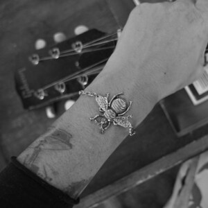 May include: A silver bee charm bracelet with a detailed bee design. The bracelet is worn on a person's wrist.