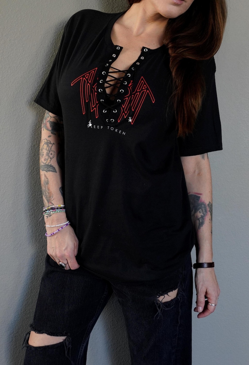 Puede incluir: Camiseta negra de gran tama&ntilde;o con un dise&ntilde;o estilizado rojo con el texto "KEEP TOKEN" debajo. La camiseta tiene un escote con cordones.