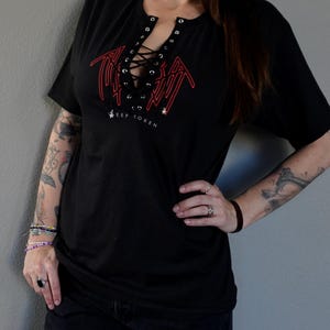 Puede incluir: Camiseta negra con un gr&aacute;fico rojo y un escote con cordones. El gr&aacute;fico presenta el texto "KEEP TOKEN".