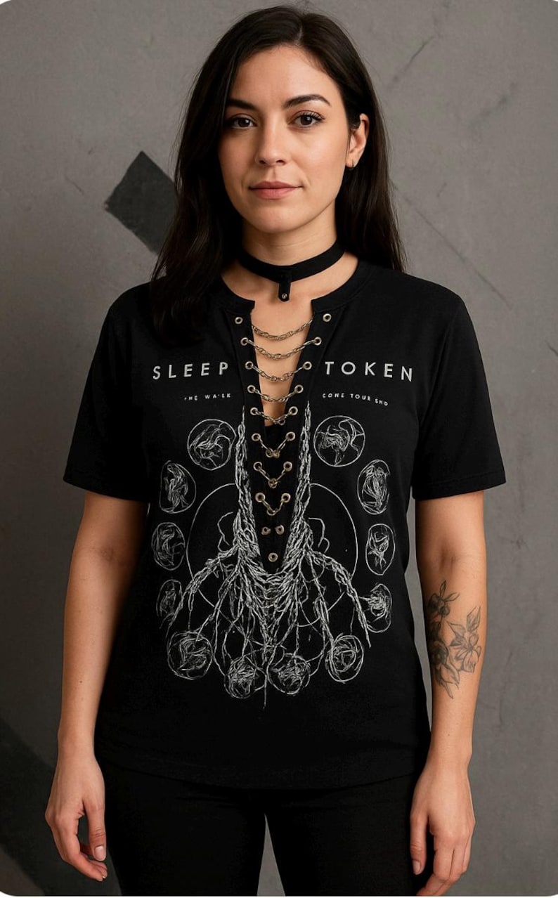 May include: Black t-shirt with the text "SLEEP TOKEN" and a graphic design. The shirt has a V-neck with chain detailing and is paired with a black choker. The design features a root-like illustration.