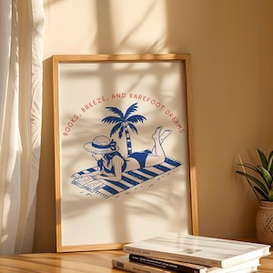 May include: A framed art print with a blue and white illustration of a person reading on a beach towel under a palm tree. The text "BOOKS, BREEZE, AND BAREFOOT DREAMS" is printed in a circular pattern around the image.