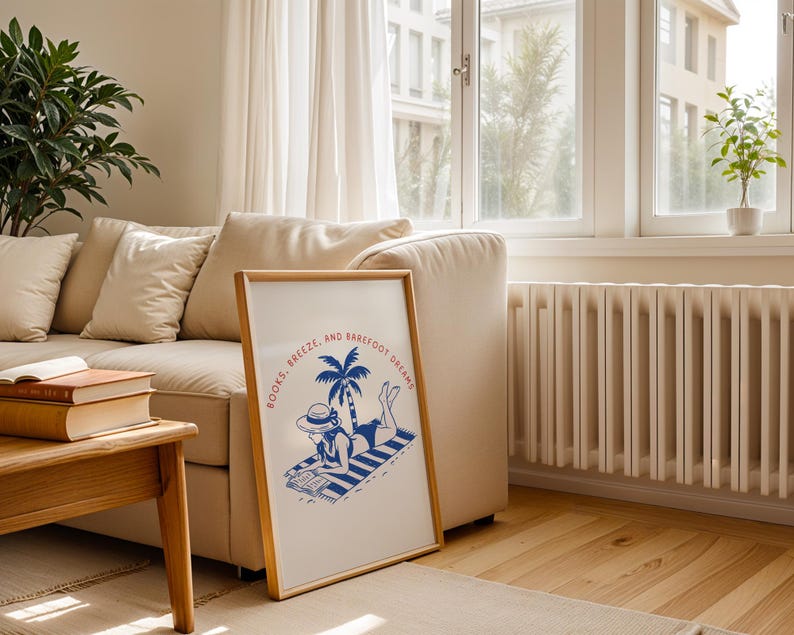 May include: A framed print with a beach scene illustration. The artwork features a person in a hat reading on a striped towel under a palm tree. The text "BOOKS, BREEZE, AND BAREFOOT DREAMS" is printed in red and blue.