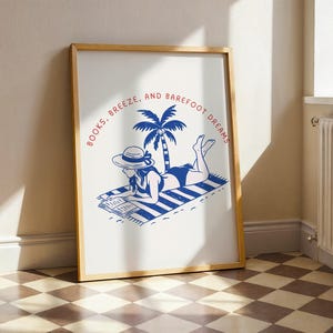 May include: Wooden framed art print with a blue and white illustration of a person reading on a beach towel. The text reads "Books, Breeze, and Barefoot Dreams" in a circular design around a palm tree.