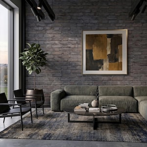 May include: A living room featuring a dark gray brick wall, a large olive green sectional sofa, two black armchairs, and a round glass coffee table. A potted fiddle leaf fig plant stands in the corner, and a framed abstract painting hangs on the wall.