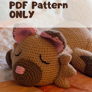 May include: A crocheted dog-shaped plush toy in shades of brown, with pink accents on the ears and nose. The dog is lying down with its eyes closed. The text "PDF Pattern ONLY" is displayed at the top.
