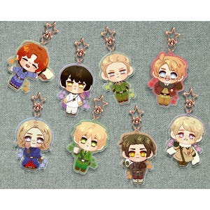 Pode incluir: Uma coleção de oito chaveiros de acrílico transparente com personagens de anime em estilo chibi vestindo uniformes de inspiração militar. Cada pingente é preso a um fecho em forma de estrela em ouro rosa e decorado com pequenos detalhes florais.