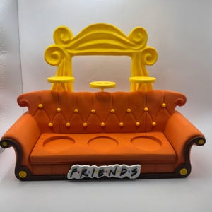 May include: An orange and brown decorative sofa with a yellow arch and three small yellow tables. The sofa has three circular cutouts and the word "FRIENDS" in the front.