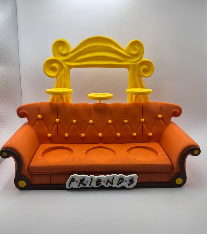 May include: An orange and brown decorative sofa with a yellow arch and three small yellow tables. The sofa has three circular cutouts and the word "FRIENDS" in the front.