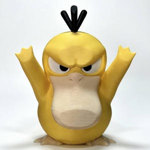 Könnte beinhalten: Eine gelbe, 3D-gedruckte Psyduck-Figur mit wütendem Gesichtsausdruck. Die Figur hat ausgestreckte Arme, einen hellbeige Schnabel und schwarzes Haar. Die Figur steht auf einer weißen Oberfläche.