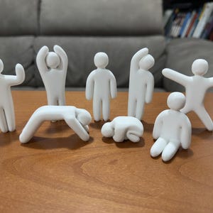 Può includere: Una collezione di otto piccole statuette bianco opaco a forma di figure umane semplificate. Ogni statuetta è rappresentata in una posizione diversa, tra cui in piedi, in fase di stretching, piegata e seduta, con superfici lisce e arrotondate.