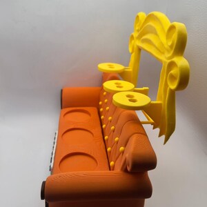 May include: An orange sofa with a yellow decorative arch and three small yellow tables. The sofa has a wooden texture, three circular cup holders, and yellow button details. The yellow arch is on the right side of the sofa.