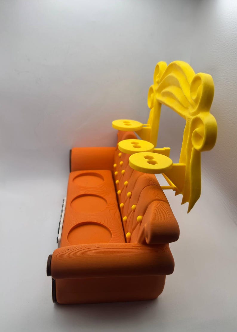 May include: An orange sofa with a yellow decorative arch and three small yellow tables. The sofa has a wooden texture, three circular cup holders, and yellow button details. The yellow arch is on the right side of the sofa.
