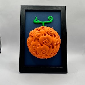 Può includere: Scultura incorniciata di un frutto arancione con uno stelo verde, simile a fiamme, su uno sfondo blu scuro. La superficie del frutto presenta intricati motivi a vortice. La cornice nera fornisce un bordo contrastante.