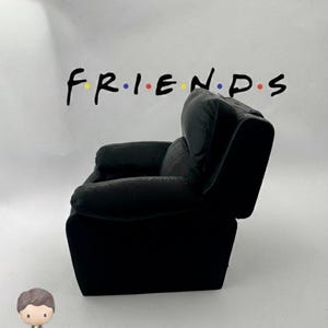 May include: A black miniature armchair with a high back and armrests. The word "FRIENDS" is written above the chair in black letters with colored dots. A small figurine of a person is in the foreground.